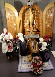 Miniaturowa kaplica ze sceną pogrzebową -- lalka w trumnie ze szklanym wiekiem, otoczona zakonnicami